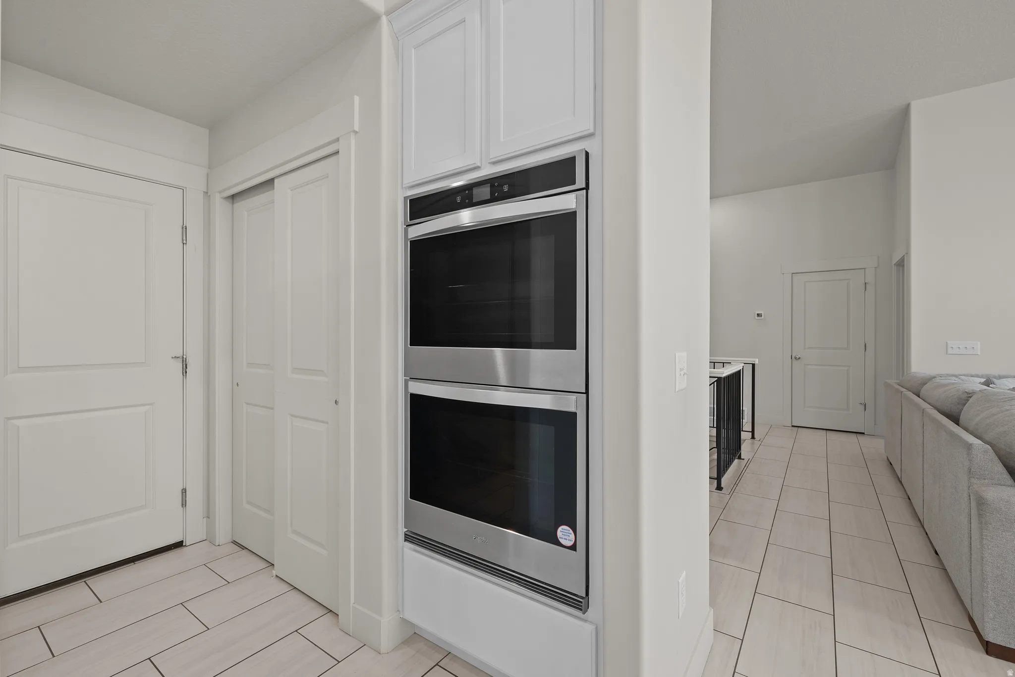 Built-in double ovens, white cabinetry, white paneled doors, white bi-fold closet doors, light-toned tile flooring