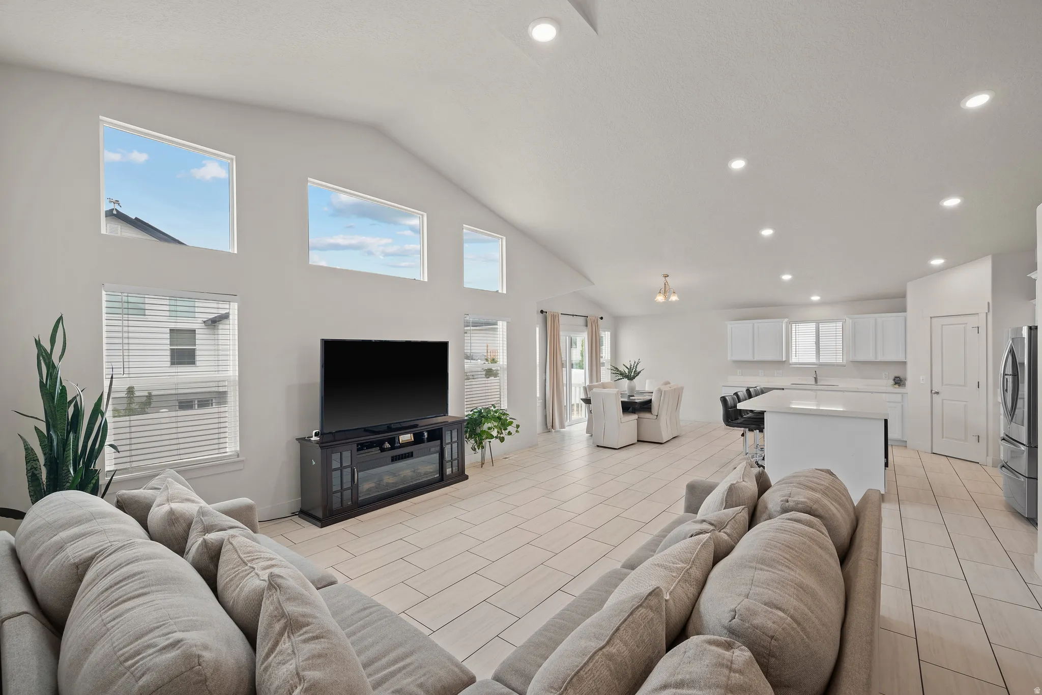 Vaulted ceilings with recessed lighting, tile flooring, modern kitchen with white cabinetry, kitchen island with counter seating, and a dining area