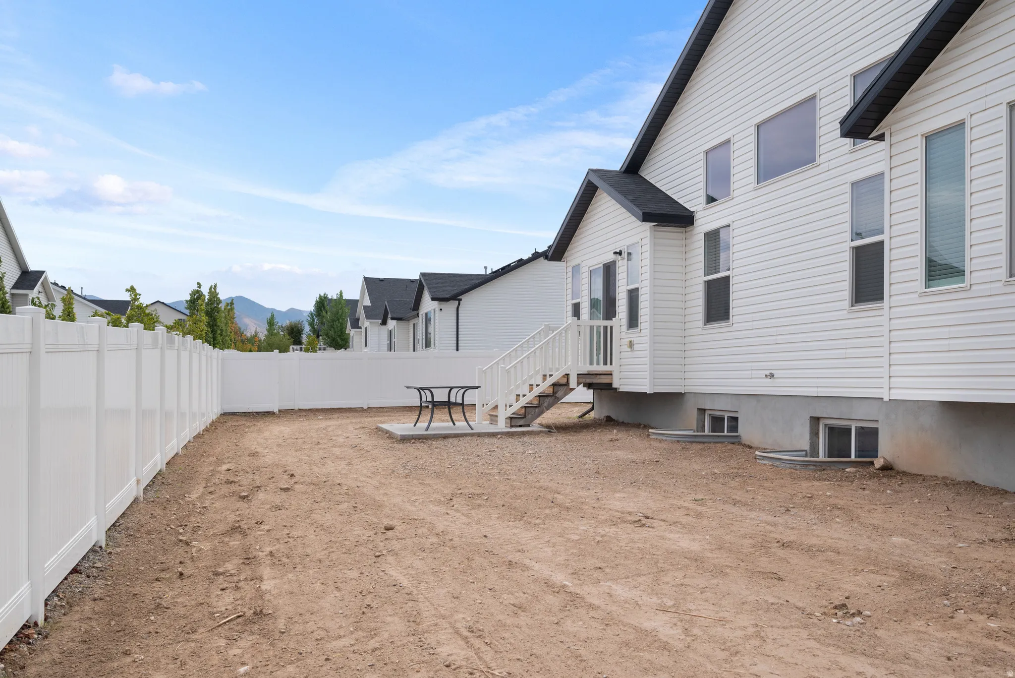 Spacious backyard with a white privacy fence, concrete patio, and exterior stairs leading to a main level door