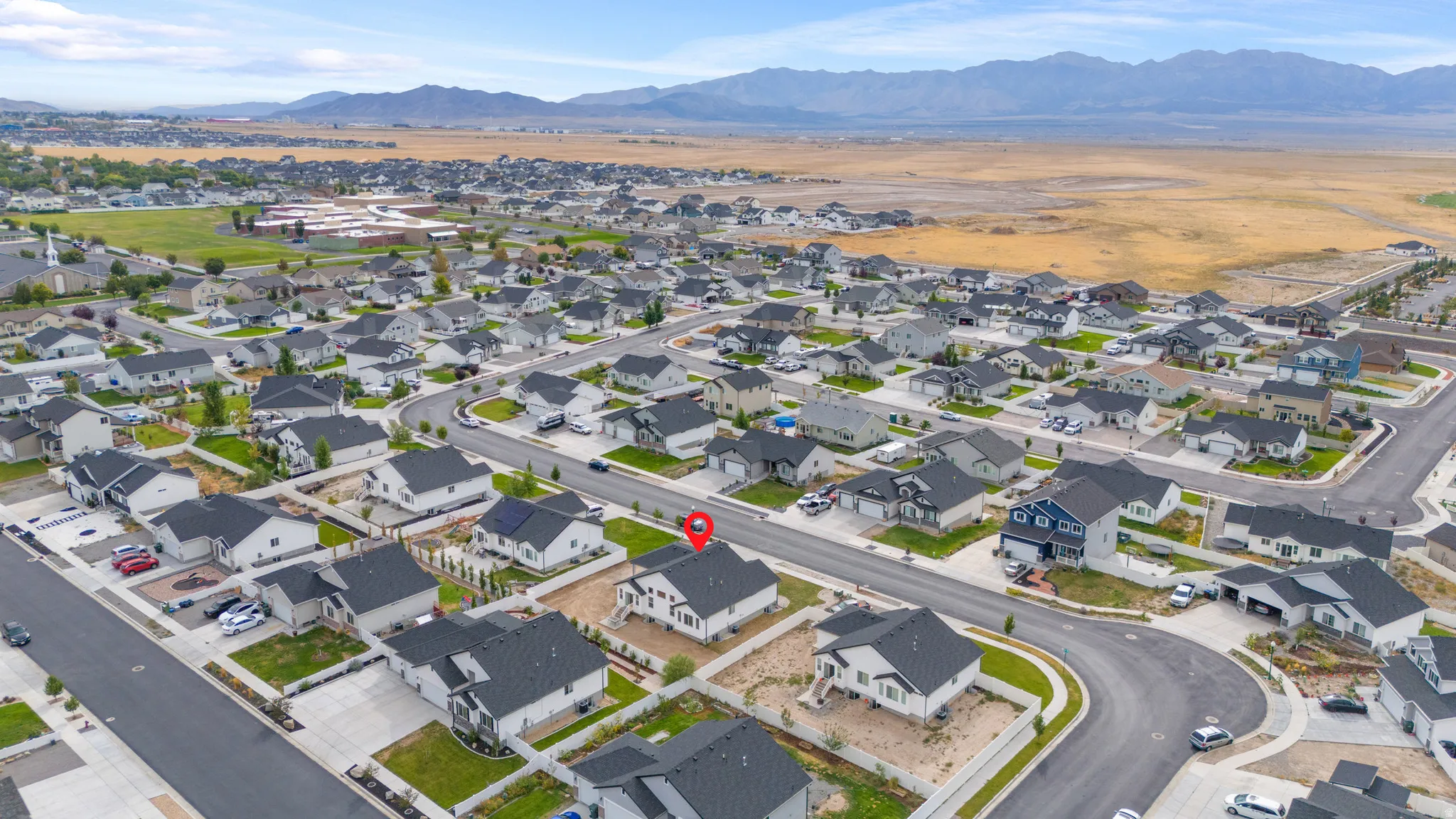 Aerial perspective of a developed residential community with diverse home designs, expansive mountain backdrop, and clear skies