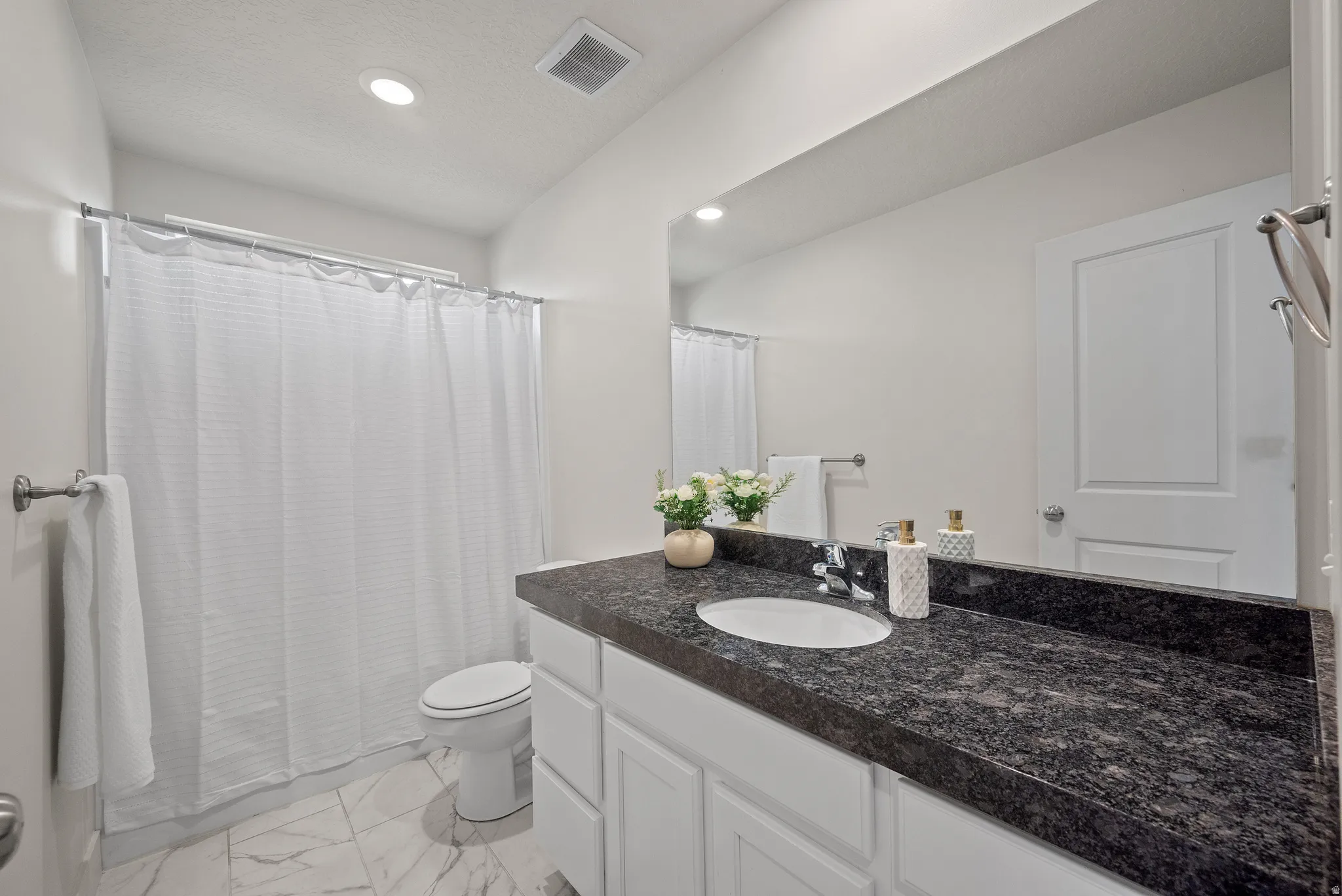 White vanity with a dark speckled countertop, undermount sink, and wall-mounted mirror
