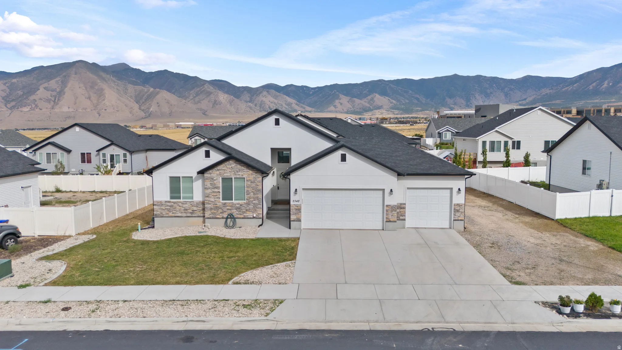 Contemporary exterior with stone and siding accents, dual garage doors, a manicured lawn, and mountain scenery