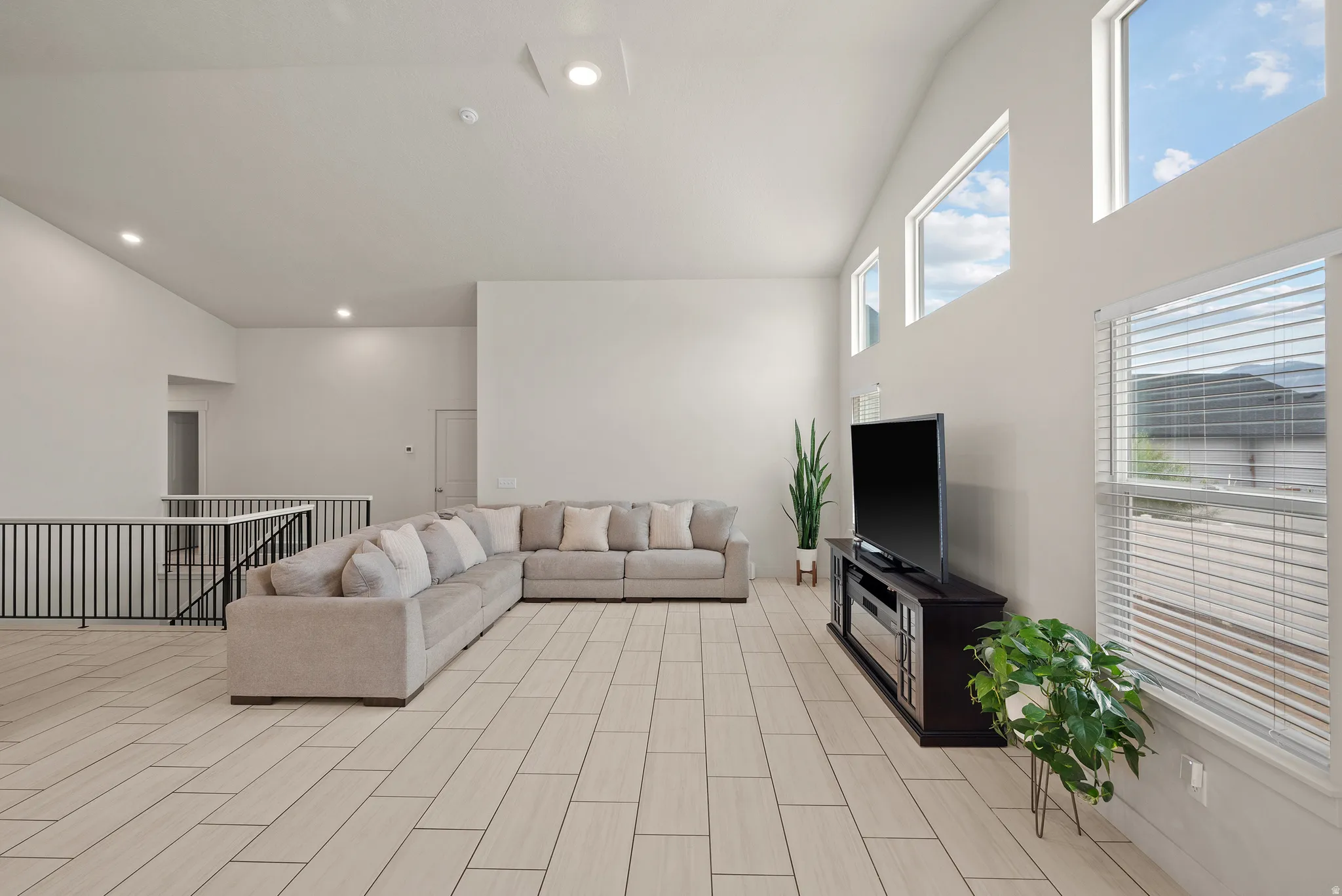 Bright, open-concept living area showcasing soaring ceilings with recessed lighting, expansive windows with plantation shutters, and neutral tile flooring throughout