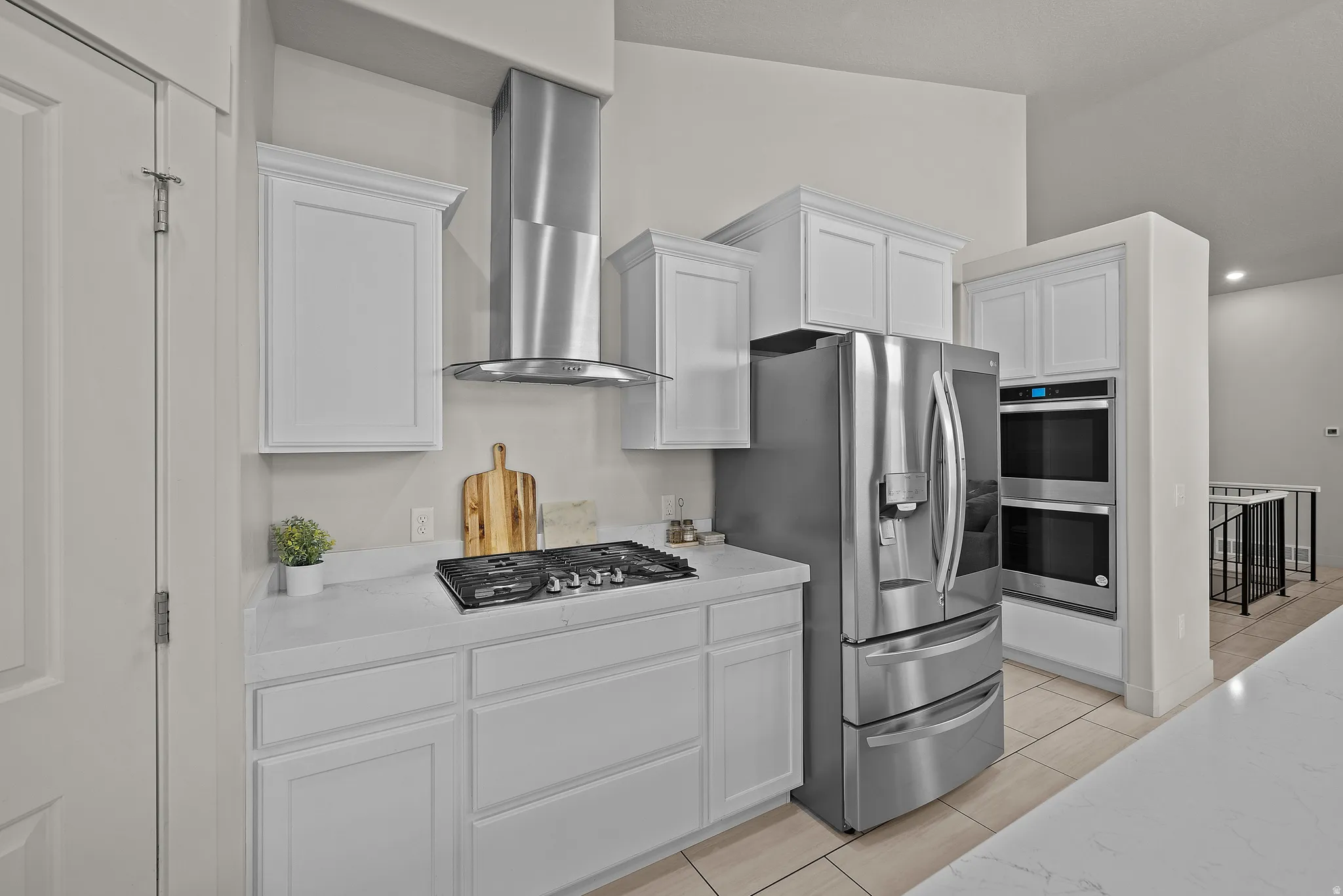 Modern kitchen featuring white shaker-style cabinetry, stainless steel French-door refrigerator with multiple compartments, gas cooktop with stainless steel range hood, and integrated wall oven