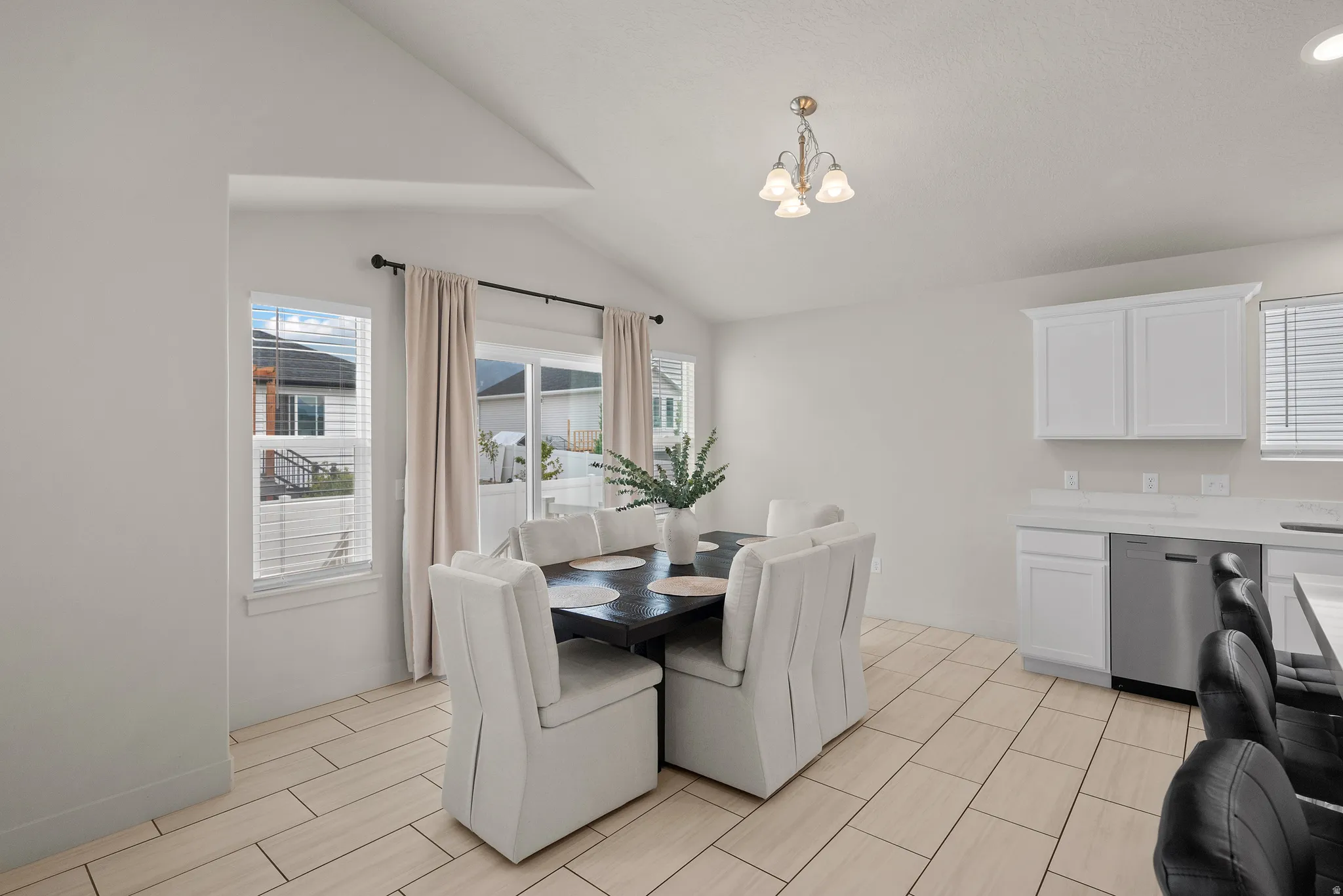 Vaulted ceiling, tile flooring, white shaker cabinetry, stainless steel dishwasher, and sliding glass door