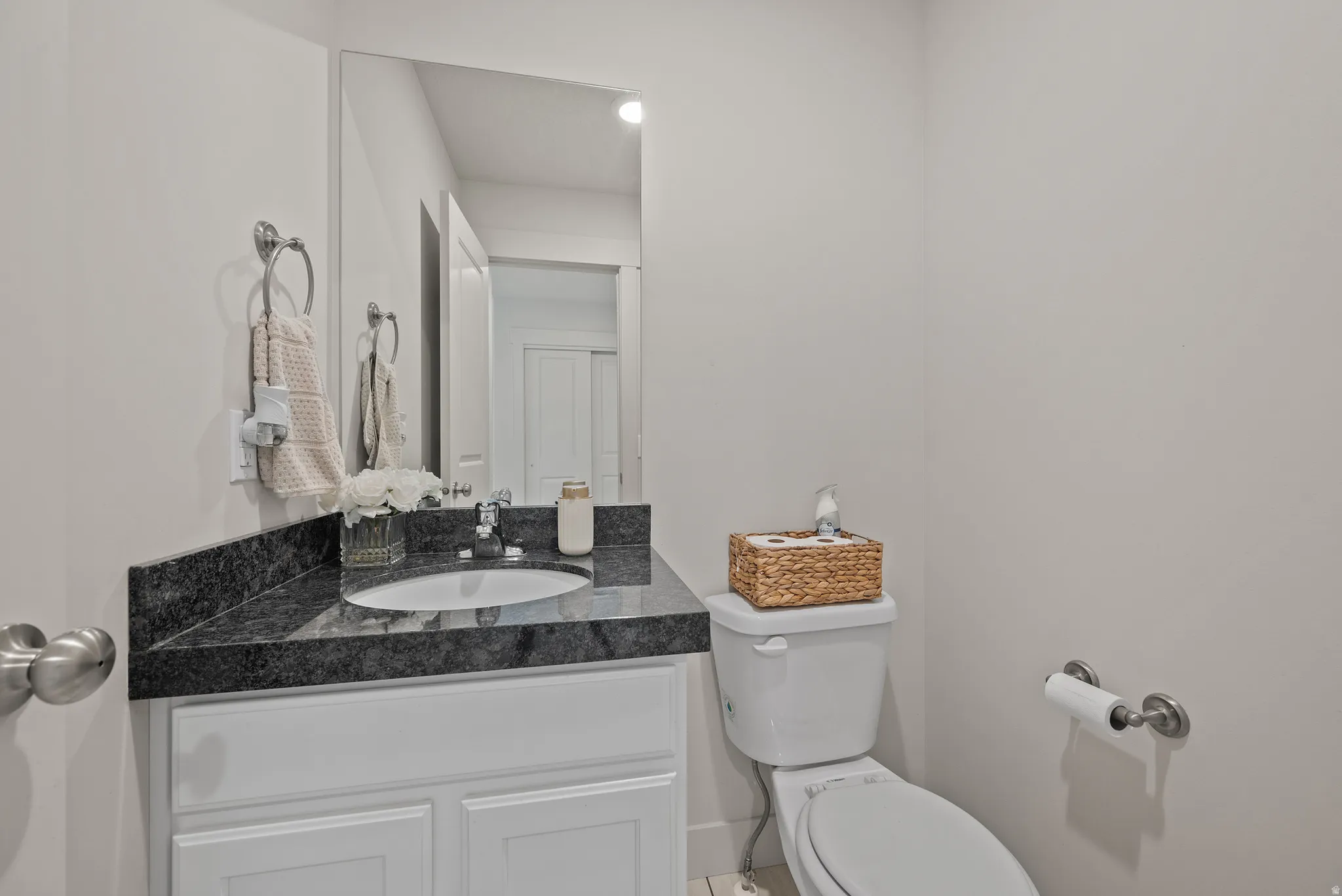 White vanity with paneled cabinetry, dark stone countertop, integrated sink, and wall-mounted mirror