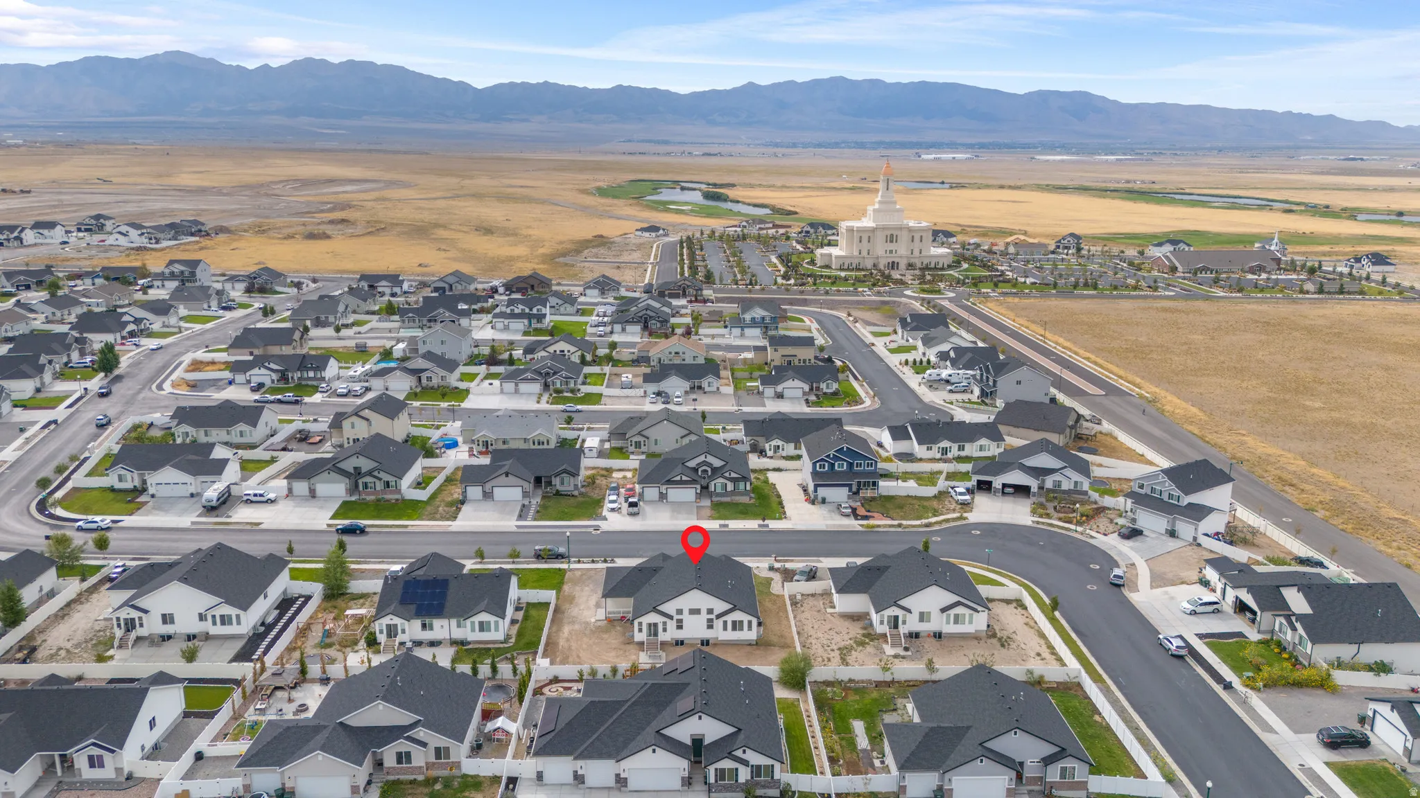 Aerial overview of the property within a residential neighborhood, featuring a distant mountainous backdrop and a prominent white architectural structure