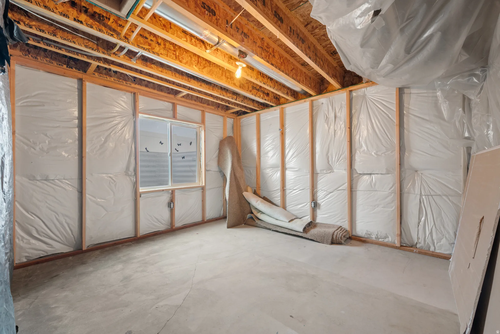 Unfinished basement space featuring exposed wooden joists, framed walls with insulation, concrete flooring, and a single window