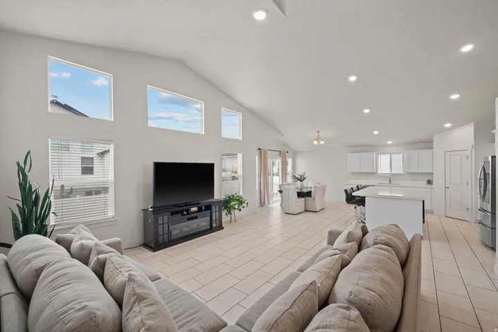 Vaulted ceilings with recessed lighting, tile flooring, modern kitchen with white cabinetry, kitchen island with counter seating, and a dining area