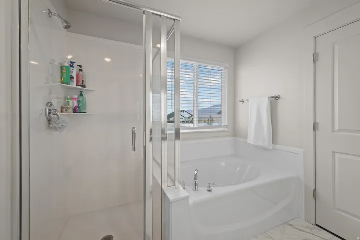 Walk-in shower with clear glass enclosure and built-in shelving, white drop-in bathtub with deck-mounted fixtures, and a window with blinds