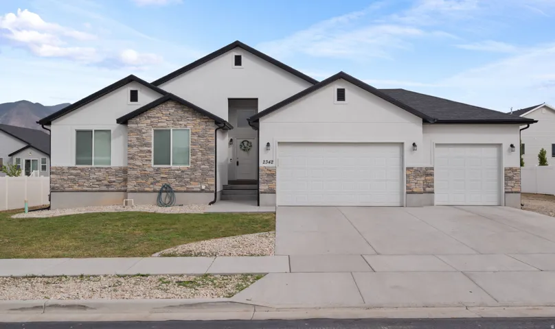 White stucco exterior with dark trim accents, featuring stone veneer detailing