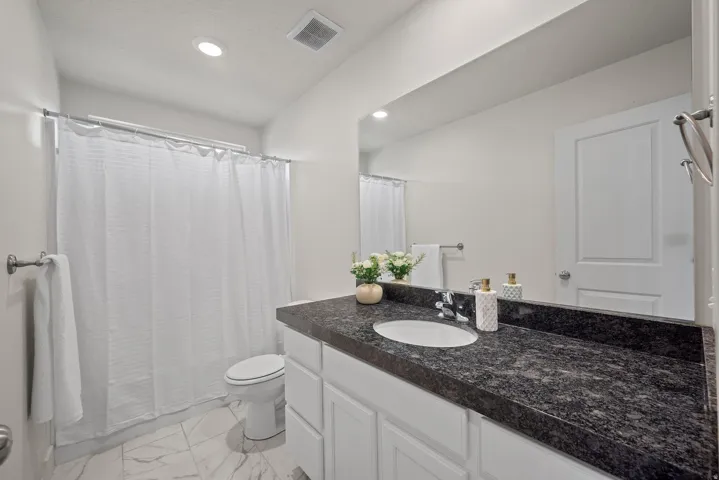White vanity with a dark speckled countertop, undermount sink, and wall-mounted mirror