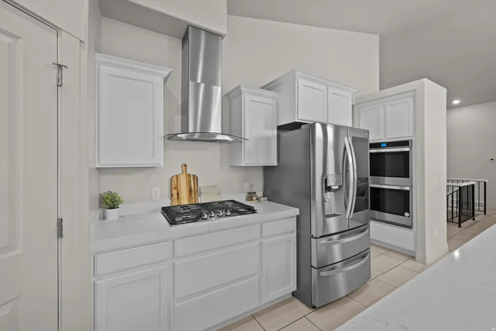 Modern kitchen featuring white shaker-style cabinetry, stainless steel French-door refrigerator with multiple compartments, gas cooktop with stainless steel range hood, and integrated wall oven