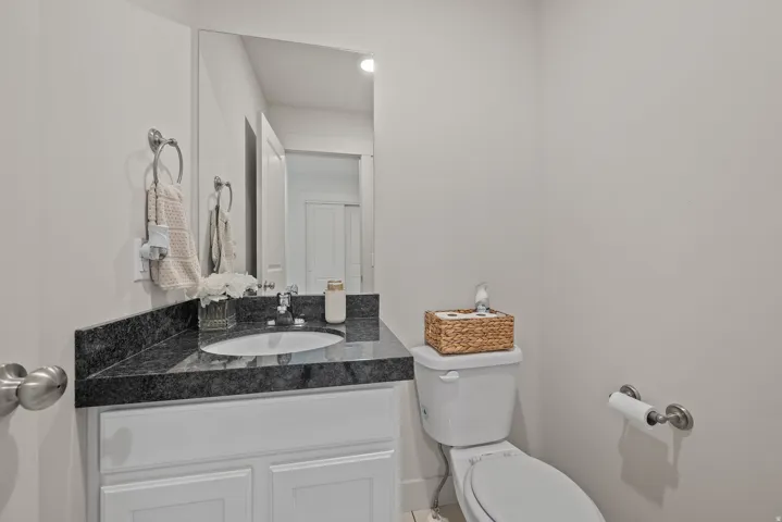 White vanity with paneled cabinetry, dark stone countertop, integrated sink, and wall-mounted mirror