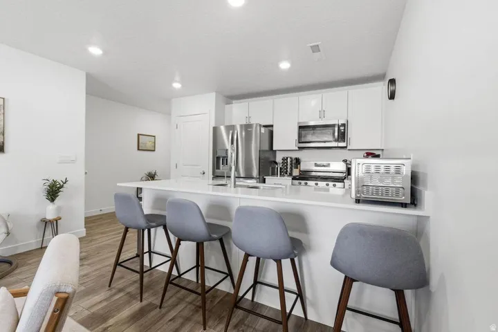 Kitchen featuring white cabinetry, stainless steel appliances, a white island with seating, recessed lighting, and wood-finish flooring