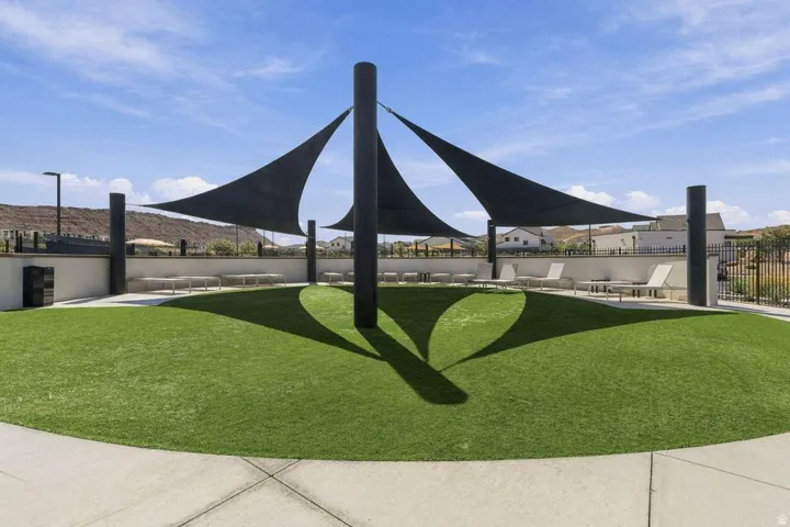 Manicured artificial turf area with multiple shade sails, perimeter concrete walkway, and a low retaining wall