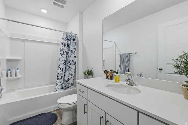 Bathroom featuring a white vanity with an undermount sink, a large wall-mounted mirror, a tub/shower combination, and wood-finish flooring
