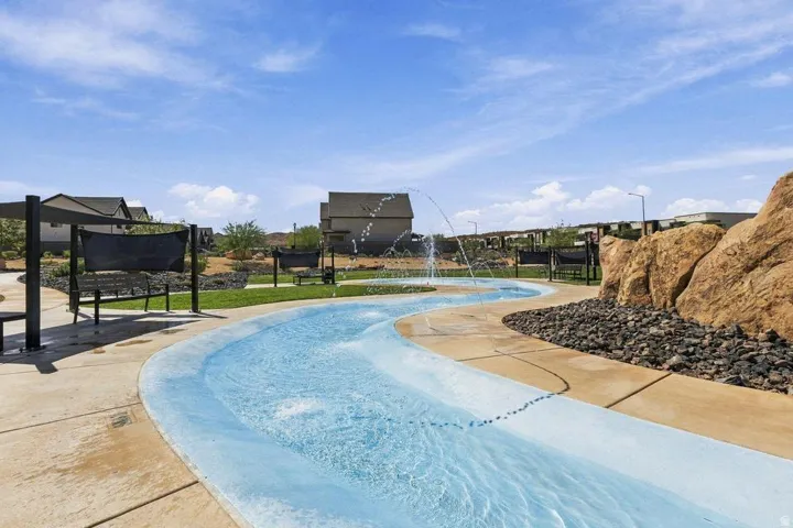 Winding water feature with integrated fountains, surrounded by paved pathways, natural rock formations, and shaded seating areas