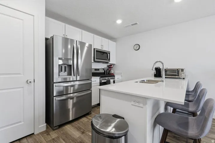Kitchen featuring stainless steel appliances, white cabinetry, a kitchen island with an undermount sink, and wood-finish flooring