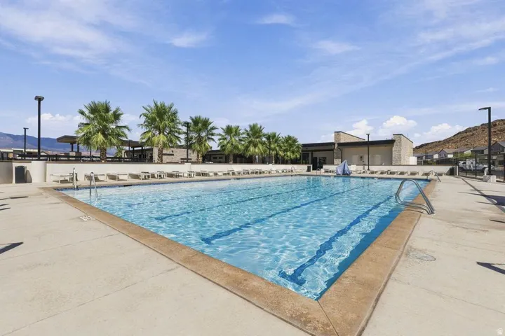 Expansive outdoor swimming pool with concrete decking, surrounding palm trees, and a distant community building