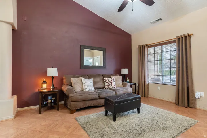 Vaulted ceiling, ceiling fan, wood-finish flooring, wall-mounted mirror, and window with blinds