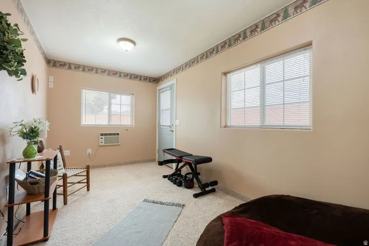 Carpeted room with a ceiling-mounted light fixture, multiple windows with blinds, and a rear exit door