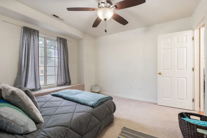 Carpeted flooring, ceiling fan with integrated lighting, wall-mounted light switch, and a paneled interior door