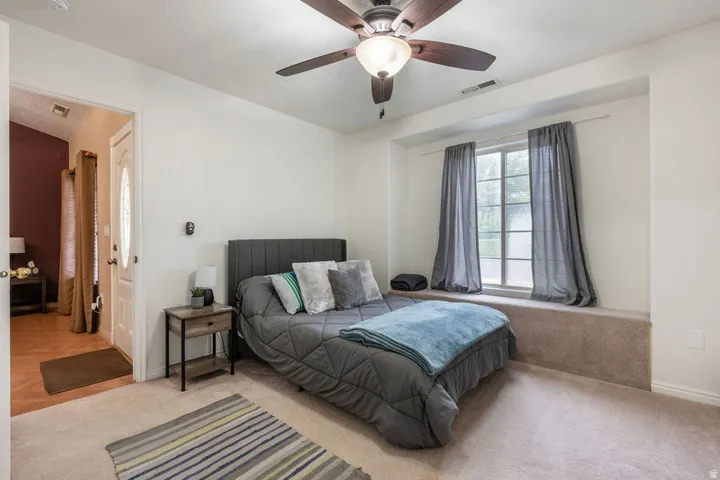 Carpeted bedroom featuring a ceiling fan with integrated lighting, a built-in window bench, and a privacy door with an oval glass insert