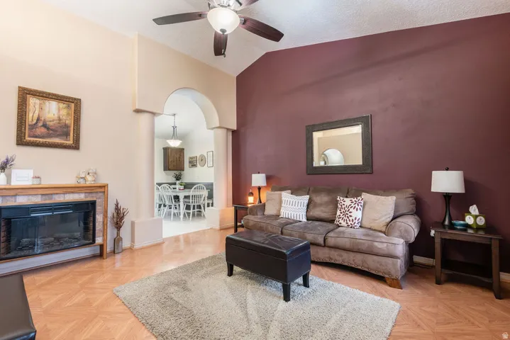 Vaulted ceiling with a ceiling fan, fireplace with a tile surround and wood mantel, arched doorway, and wood-finish flooring