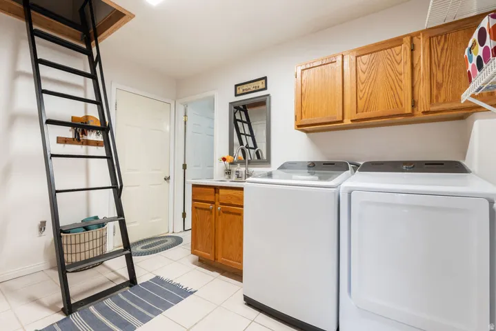 Laundry area with ceramic tile flooring, wood cabinetry, and a utility sink