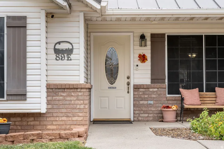 Fiberglass front door with oval-shaped decorative glass, a metal roof, brick veneer siding, and a concrete walkway