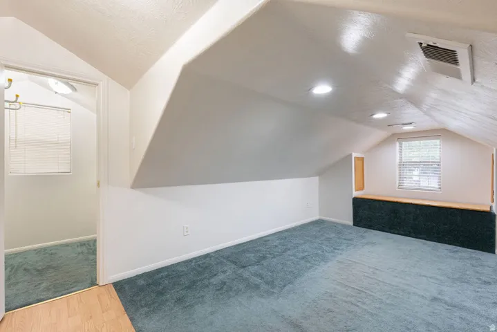 Vaulted ceiling with recessed lighting, integrated window seat, and blue carpeting