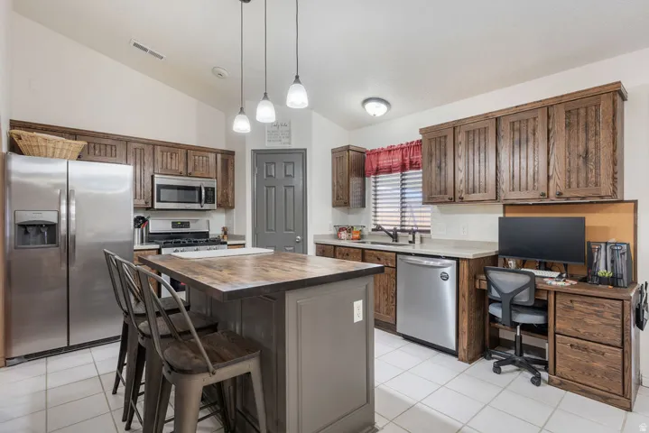 Vaulted ceiling, wood-finish cabinetry, stainless steel appliances, central island with wood-finish countertop, and integrated desk space