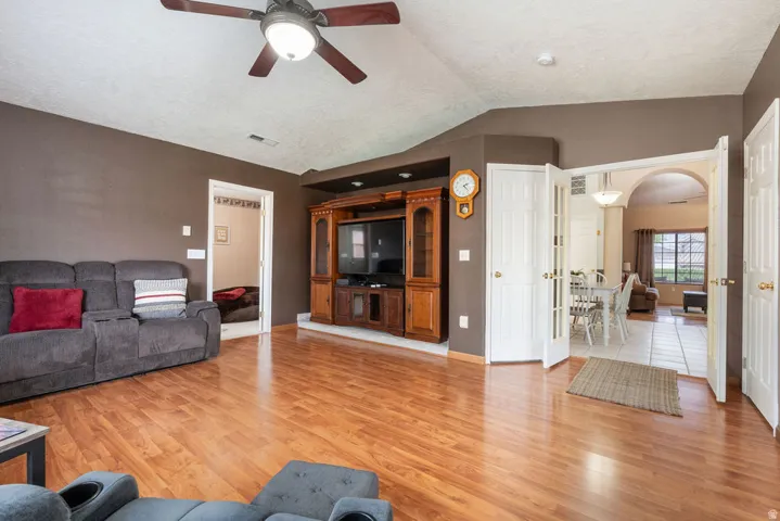 Wood-finish flooring, ceiling fan, and French doors leading to a tiled dining area