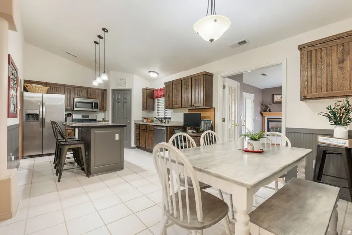 Kitchen featuring a center island, stainless steel appliances, wood-finish cabinetry, tile flooring, and a dining area with a chandelier