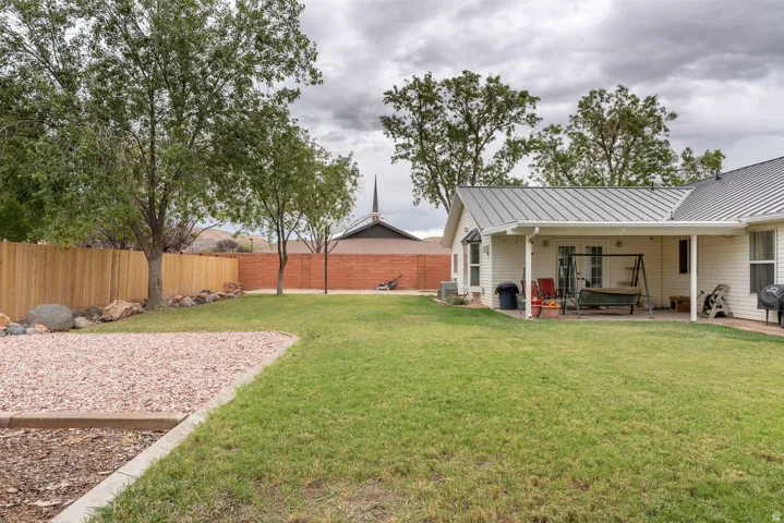 Expansive backyard featuring a covered patio, metal roof, and a wood privacy fence