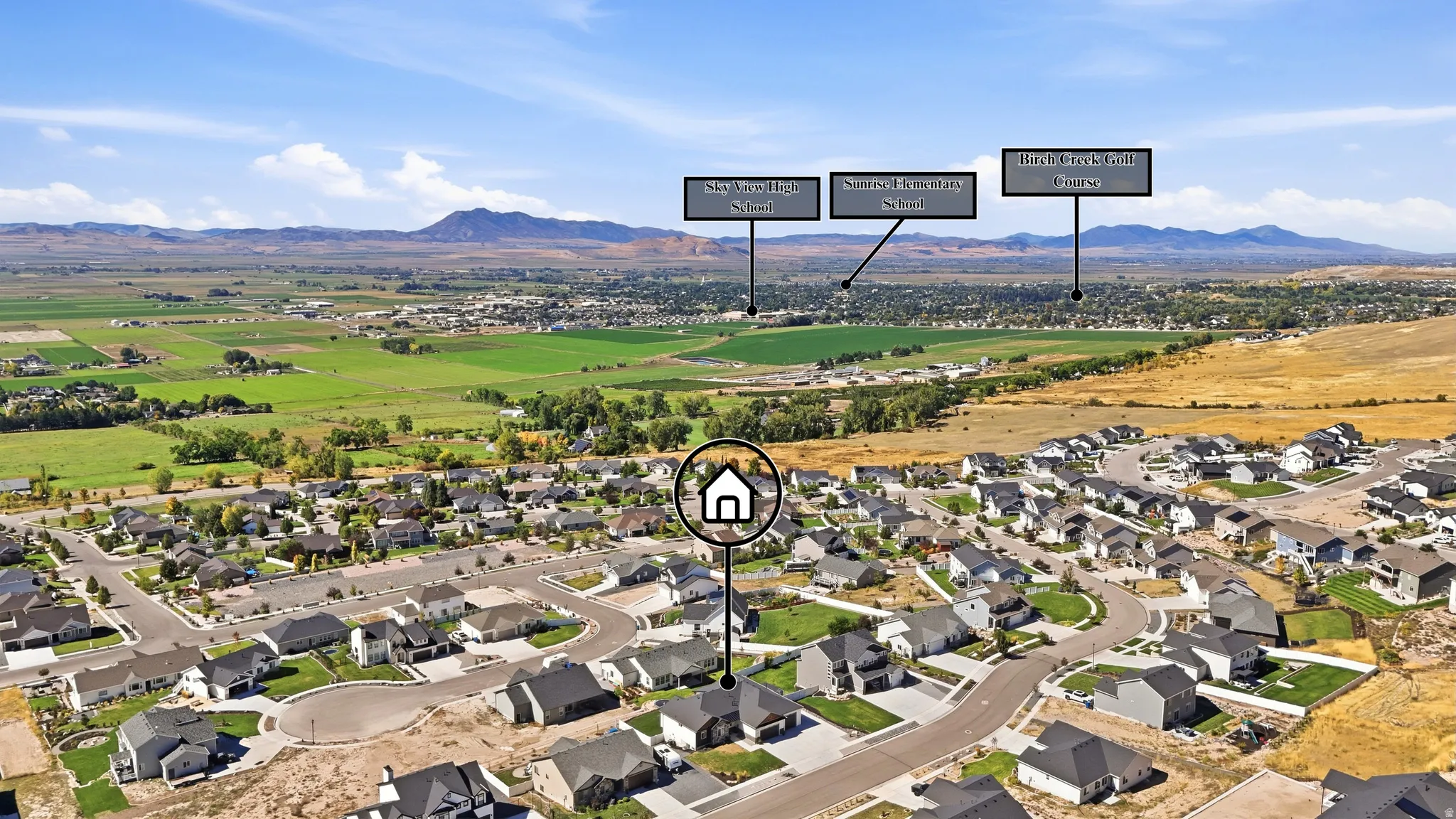 Aerial perspective showcasing a residential neighborhood with surrounding open fields and distant mountains