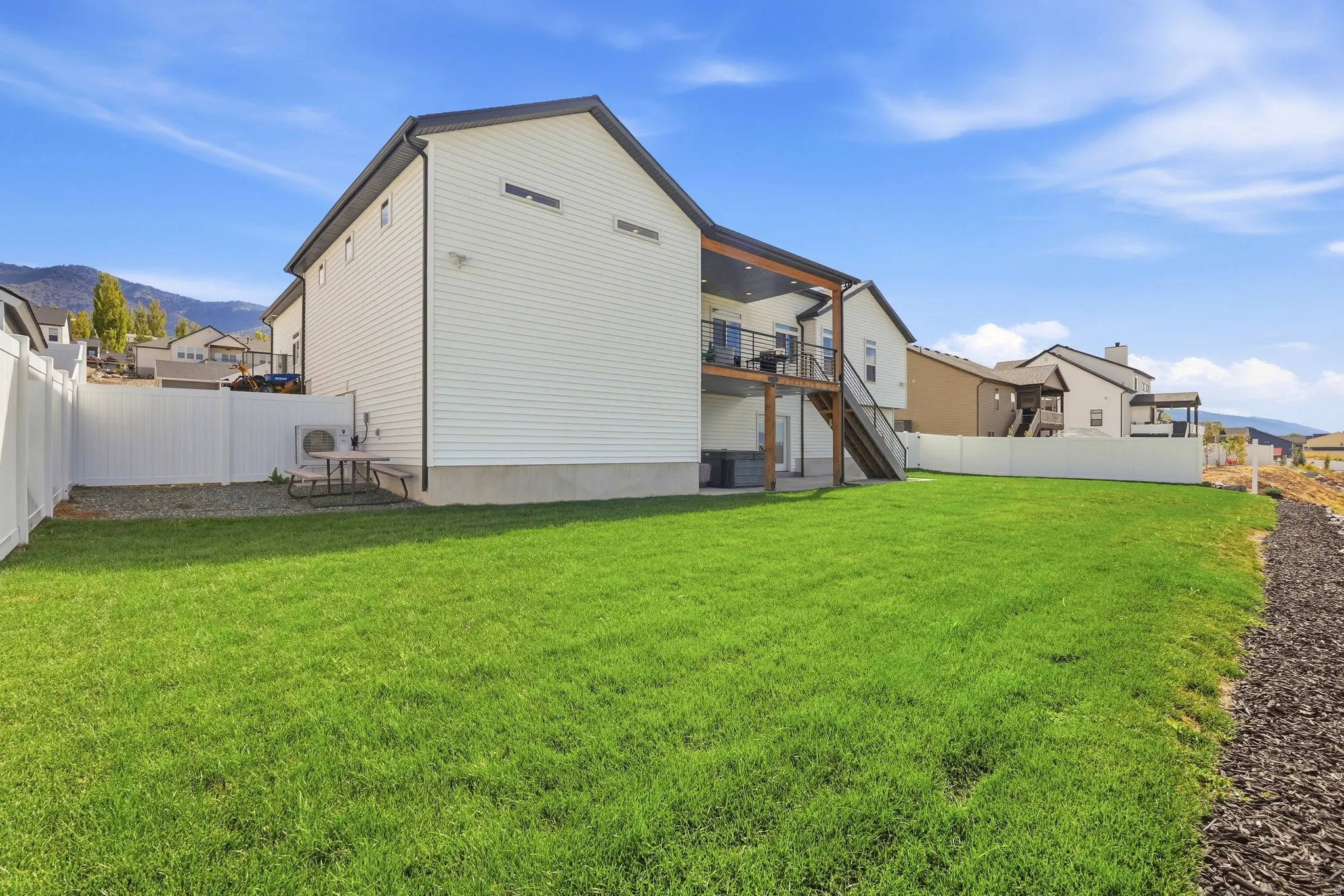 Expansive backyard featuring a manicured lawn, a white privacy fence, and a multi-level deck with a covered upper portion