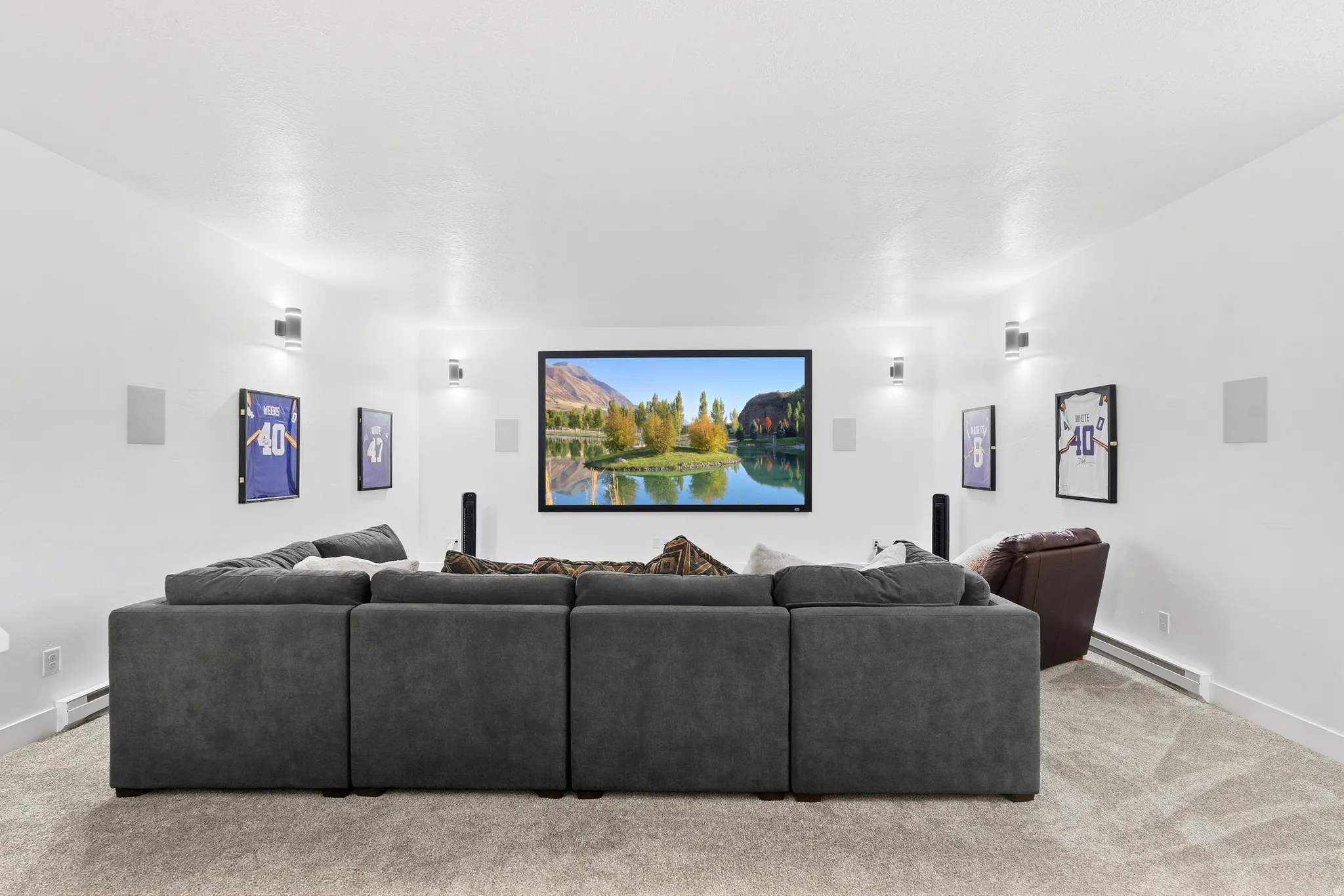 Carpeted media room with recessed lighting, integrated wall speakers, wall-mounted sconces, and a large display screen