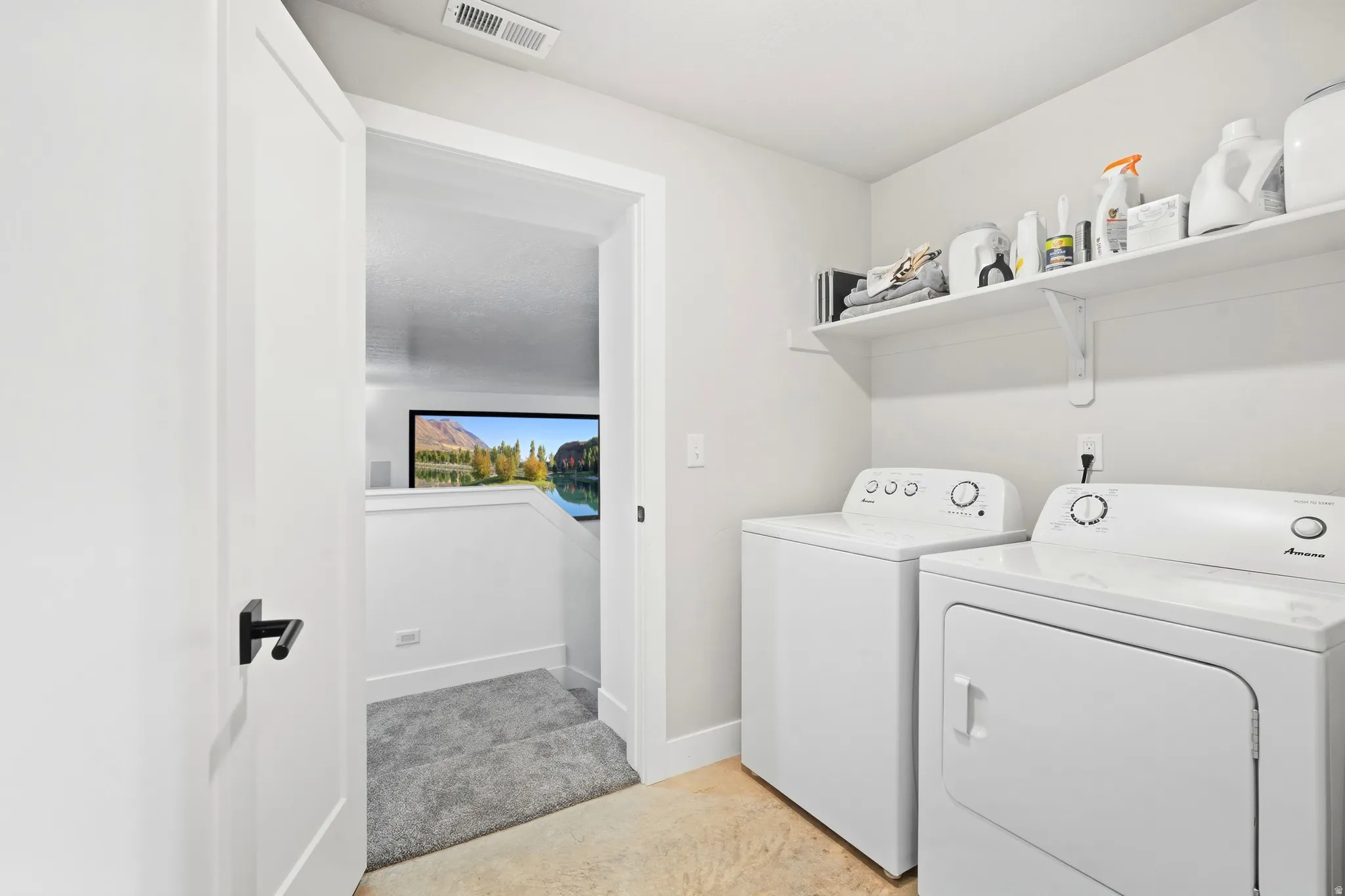 White washer and dryer appliances, wall-mounted shelving, and a clean white door with a black handle