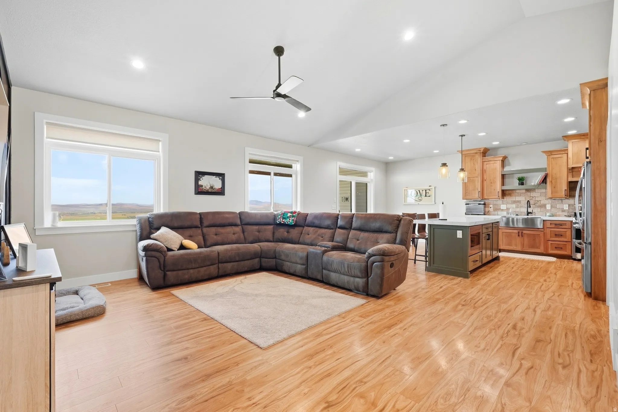Vaulted ceiling with a ceiling fan, recessed lighting, wood-finish flooring, windows with roller shades, and a kitchen featuring a central island with pendant lighting