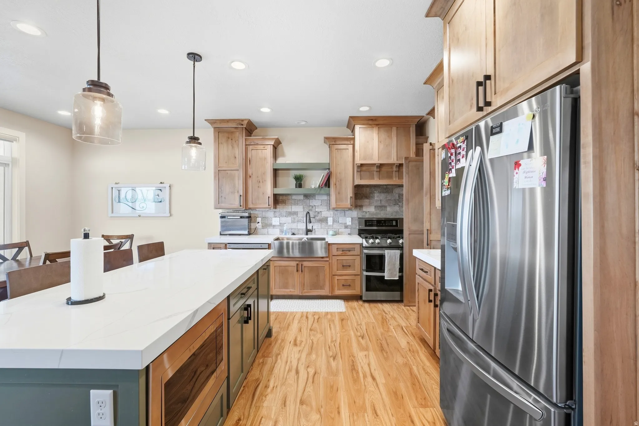 Chef's kitchen featuring custom wood cabinetry, stainless steel appliances including a French-door refrigerator and dual wall ovens, white quartz countertops, and a large center island with seating