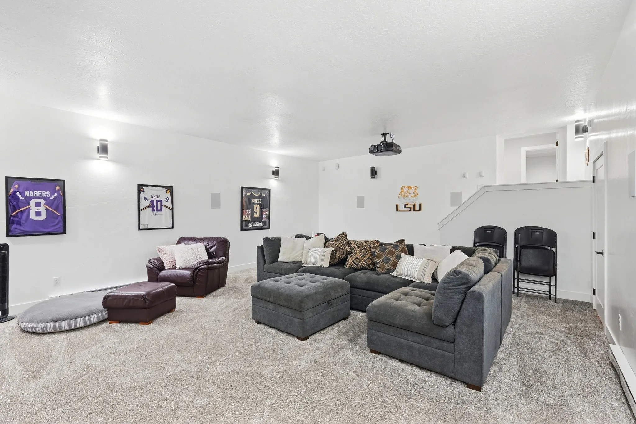 Carpeted living area featuring recessed lighting, wall-mounted light fixtures, a ceiling-mounted projector, and integrated wall speakers