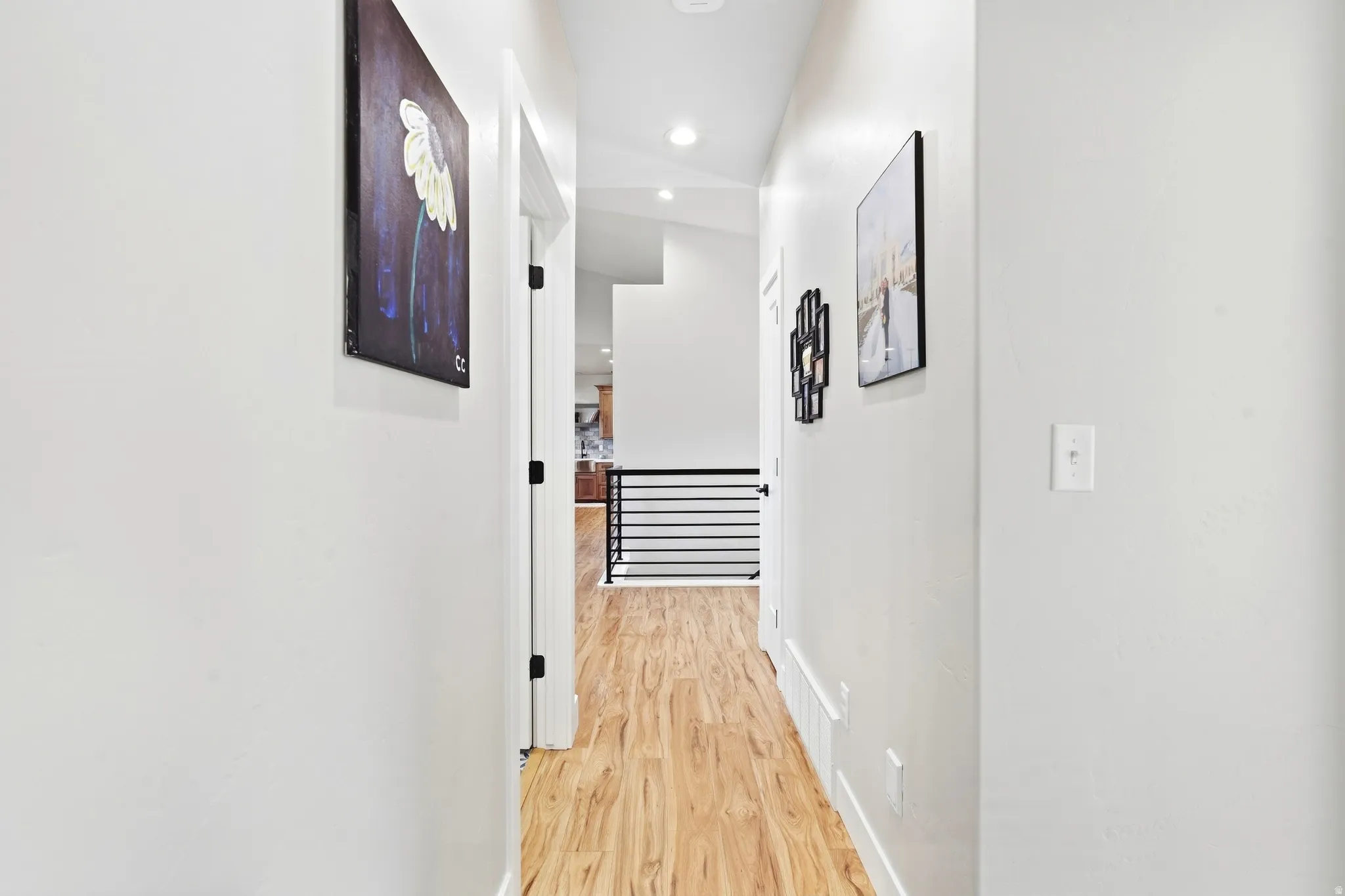 Hallway featuring wood-finish flooring, white walls, recessed lighting, and black metal railings