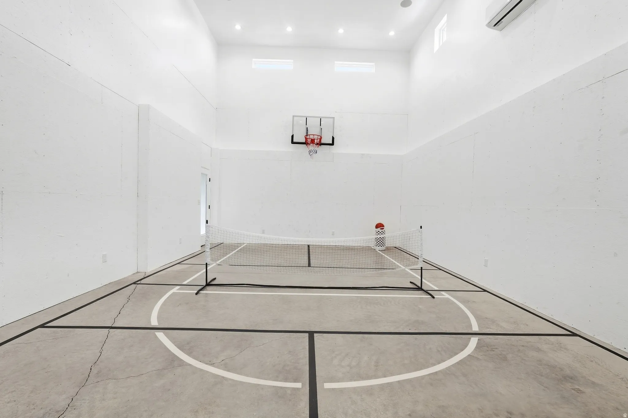 Indoor sports court with concrete flooring, high ceilings, recessed lighting, and a wall-mounted basketball hoop