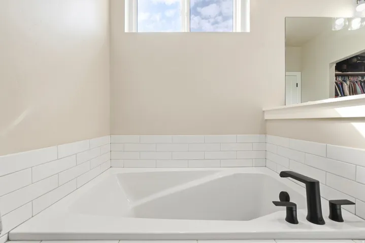 Built-in soaking tub with modern matte black fixtures and white subway tile surround