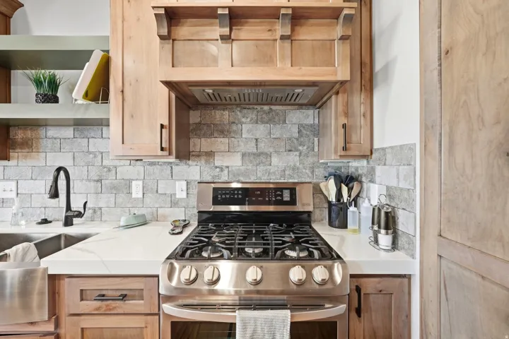 Stainless steel range, wood-finish cabinetry, quartz countertops, subway tile backsplash, and a black gooseneck faucet