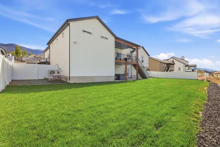 Expansive backyard featuring a manicured lawn, a white privacy fence, and a multi-level deck with a covered upper portion