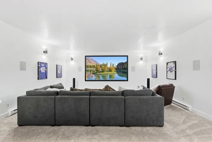 Carpeted media room with recessed lighting, integrated wall speakers, wall-mounted sconces, and a large display screen