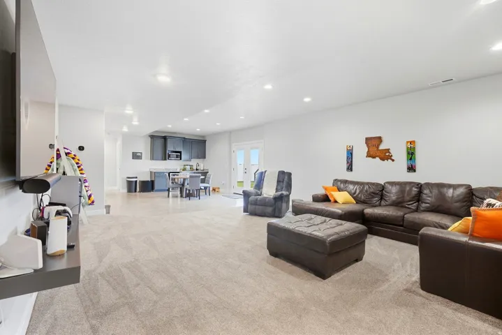 Expansive carpeted living area with recessed lighting, featuring a built-in wet bar with dark cabinetry, integrated dining area, and double doors providing exterior access